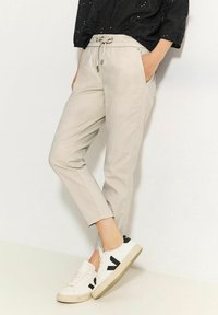 Ljusgrå tapered byxor med elastisk midja och dragsko, tillsammans med vita sneakers med svarta accenter och logotyper.