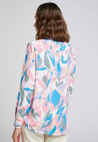 Blouse à motif floral en tissu léger, avec des teintes rose, bleu, vert et lavande, dotée de manches longues et de poignets boutonnés.