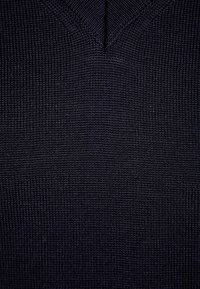 Dunkelblauer Strickpullover mit einem strukturierten V-Ausschnitt-Design, ribbelmuster und subtilen Variationen im Stoffgewebe.