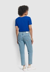 Camiseta de manga corta azul real con escote en la espalda, acompañada de jeans de tiro alto azul claro y zapatillas blancas.