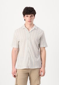 Camisa de botones de manga corta en colores claros con patrón ondulado; cuenta con un cuello y una tela suave y texturada.