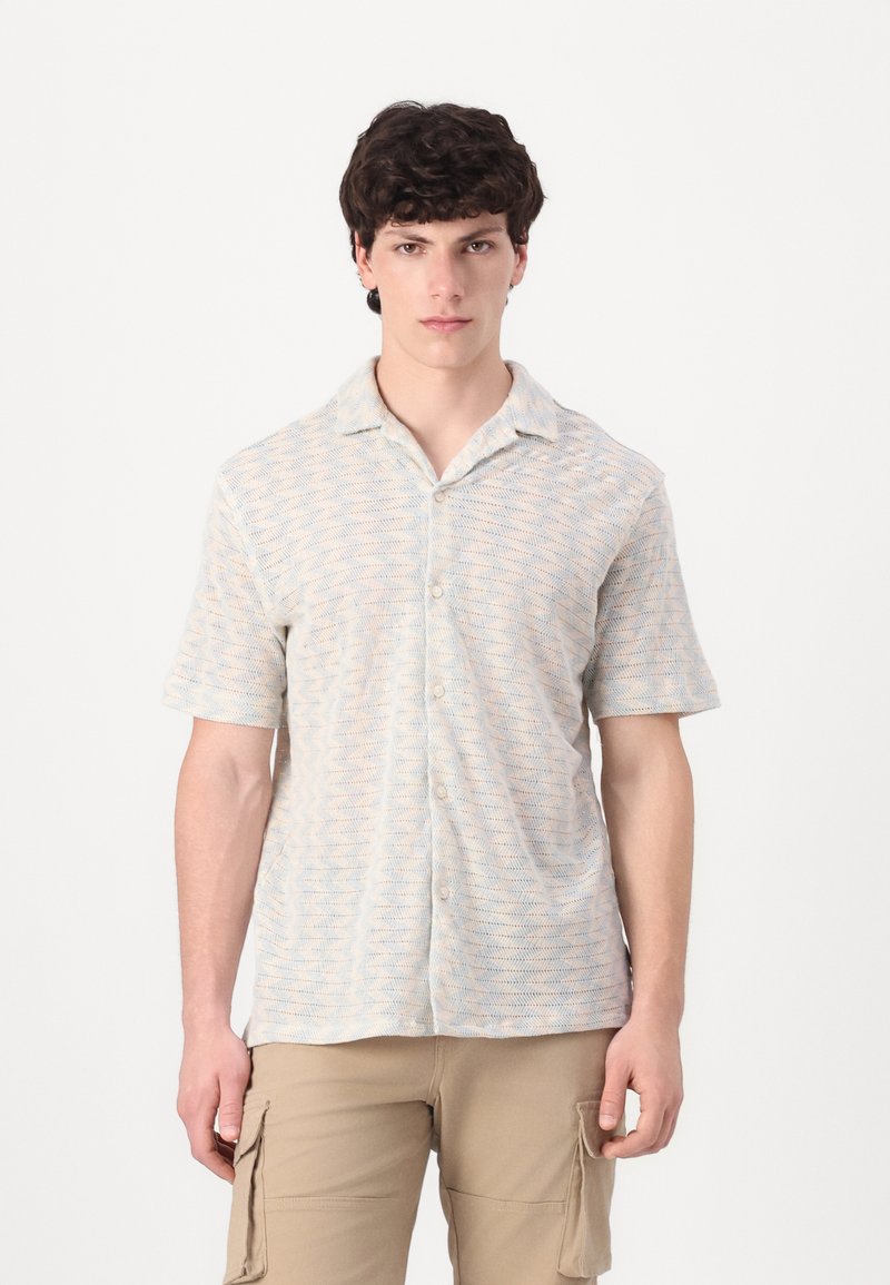 Camisa de botones de manga corta en colores claros con patrón ondulado; cuenta con un cuello y una tela suave y texturada.