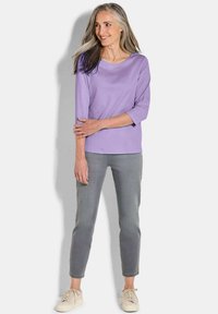 Lavendelkleurig langomarm T-shirt met een ronde hals, gecombineerd met grijzige tapered broek en beige sneakers, wat het zachte materiaal en de ontspannen pasvorm benadrukt.