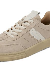 Beżowe zamszowe tenisówki z białymi akcentami, posiadające płaskie sznurowadła, przeszycia oraz gumową podeszwę. Lekko fakturowana cholewka.