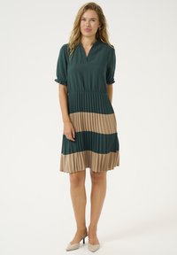 Zelena nabrana obleka s kratkimi pufastimi rokavi, ki ima na dnu bež vodoravno črto. Narejena je iz gladkega materiala z ohlapnim krojem.