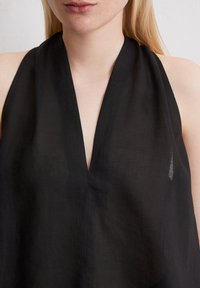 Top noir sans manches avec un décolleté en V profond et un tissu léger et transparent. Le design est minimaliste, sans motifs ni embellissements supplémentaires.