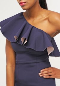Robe asymétrique bleu marine avec un col volanté ; tissu lisse ; présente une doublure rose clair sur le volant ; corsage ajusté.