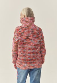 Kootud kampsun erksates mitmevärvilistes mustrites, kõrge krae, paksudest lõngadest tekstuuridega, pikad varrukad ja lõdvestunud lõige.