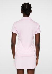 Rosa pikétröja med korta ärmar och krage, med vita sidoseam och en matchande kjol, tillverkad av ett slätt, stretchigt material.