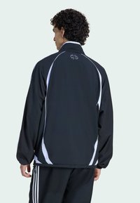 Melns žakets ar baltām akcentiem, viegls dizains, augsta apkakle un elastīgas aproces. Aizmugurē ir logotips un gluda tekstūra.