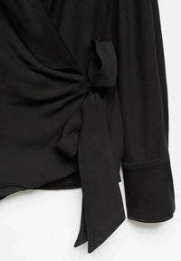 Blusa nera con design avvolgente, caratterizzata da un accento con nodo legato sul lato e maniche lunghe con una texture liscia e fluida.