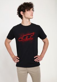 Černé bavlněné tričko s logem "JT Racing" v červené barvě se efektem rozstřiku, kulatým výstřihem a krátkými rukávy. Nosit s světlými béžovými kalhotami.
