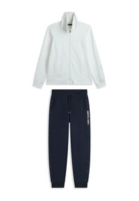 Giacca bianca con zip e colletto alto, abbinata a pantaloni joggers blu navy con coulisse e dettagli laterali. Scritta "FREDDY TRAINING" stampata sui pantaloni.