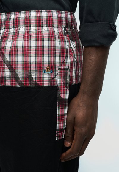 Κοντινό πλάνο ενός σκούρου δέρματος χεριού δίπλα σε κόκκινη και λευκή καρό μέση με κεντημένο λογότυπο σε μαύρα ρούχα.