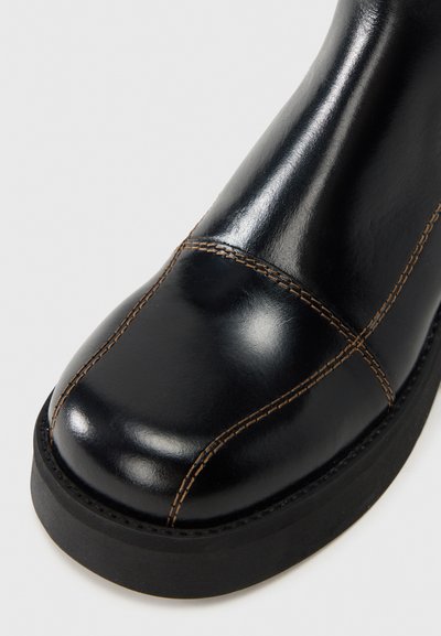 Μαύρη δερμάτινη μπότες με στρογγυλεμένη μύτη, αντίθετες καφέ ραφές, ομαλή υφή και μαύρη ελαστική σόλα.