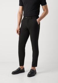 Černé tapered kalhoty vyrobené z hladkého materiálu, s plochým předním dílem, bočními kapsami a klasickým zapínáním na knoflík.