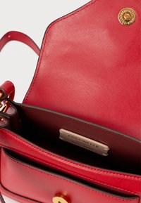 Κόκκινη δερμάτινη τσάντα χειρός με ανοιχτό καπάκι, κλείσιμο με χρυσό κουμπί και εσωτερική ετικέτα που αναγράφει "Coccinelle Authentic Italian Leather".