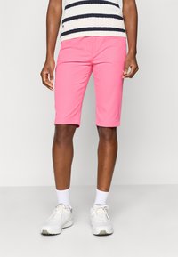 Calções cor-de-rosa com uma textura suave, que chegam um pouco acima do joelho. Em combinação com ténis brancos e meias brancas até ao tornozelo. Camisola com riscas horizontais.