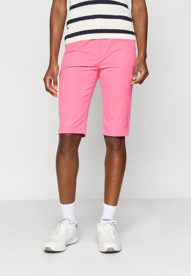 Calções cor-de-rosa com uma textura suave, que chegam um pouco acima do joelho. Em combinação com ténis brancos e meias brancas até ao tornozelo. Camisola com riscas horizontais.