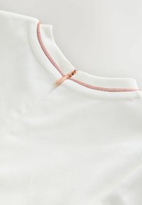 Weißer, strukturierten Stoff mit runder Ausschnitt, ausgestattet mit einem roségoldenen Reißverschluss und kontrastierenden roségoldenen Fadenakzenten am Kragen.