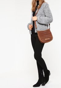 Brązowa torebka na ramię o prążkowanej fakturze i mocnym pasku, w zestawieniu z grubym szarym swetrem, czarną bluzką i czarnymi legginsami.