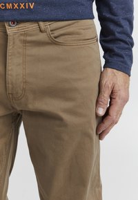 Khaki Baumwollhosen mit geradem Schnitt, sichtbaren Nähten, Fünf-Taschen-Design und vorderem Knopfverschluss.