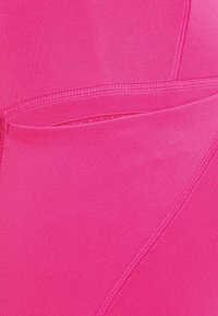 Fuchsiové sportovní legíny s hladkým povrchem, vybavené boční kapsou a kontrastním šitím pro zvýraznění detailu.