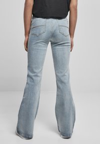 Ljusblå utsvängda jeans med medelvattning, med två bakfickor och synliga sömnadsdetaljer. Texturen är slät och liknar denim.