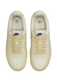 Sneakers Nike in pelle crema pallido. Le caratteristiche includono punta perforata, lacci morbidi e logo. Suola testurizzata. Design minimalista.