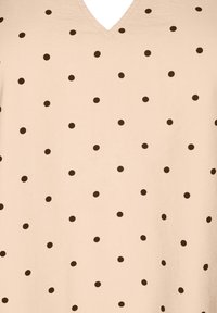 Beige V-Ausschnitt-Top mit gleichmäßig verteilten braunen Punkten, aus weichem Stoff mit glatter Textur.