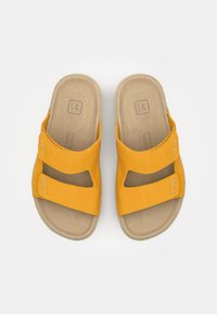 Keltaiset huopasandaalit, joissa on kaksi leveää hihnaa ja vaalea pohja. Hihnassa on ommeltu yksityiskohta ja pohjassa logojälki.