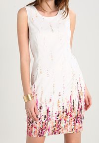 Robe blanche sans manche avec des motifs abstraits colorés en rose, orange et noir au bas. Tissu doux avec une silhouette ajustée.