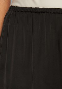 Black elastic waist skirt with a soft, flowing texture, featuring subtle pleats and a smooth finish, designed for comfort and ease of movement.