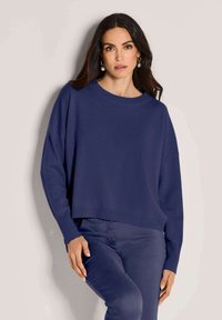 Dunkelblaues Strickpullover mit rundem Ausschnitt, überschnittenen Schultern und gerippten Bündchen, kombiniert mit passenden, schmal geschnittenen Hosen.