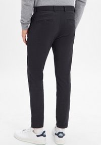 Ciemnoszare slim-fit spodnie wykonane z gładkiego materiału, z płaskim przodem, bocznymi kieszeniami i dwiema tylnymi kieszeniami. W połączeniu z białymi sneakersami.