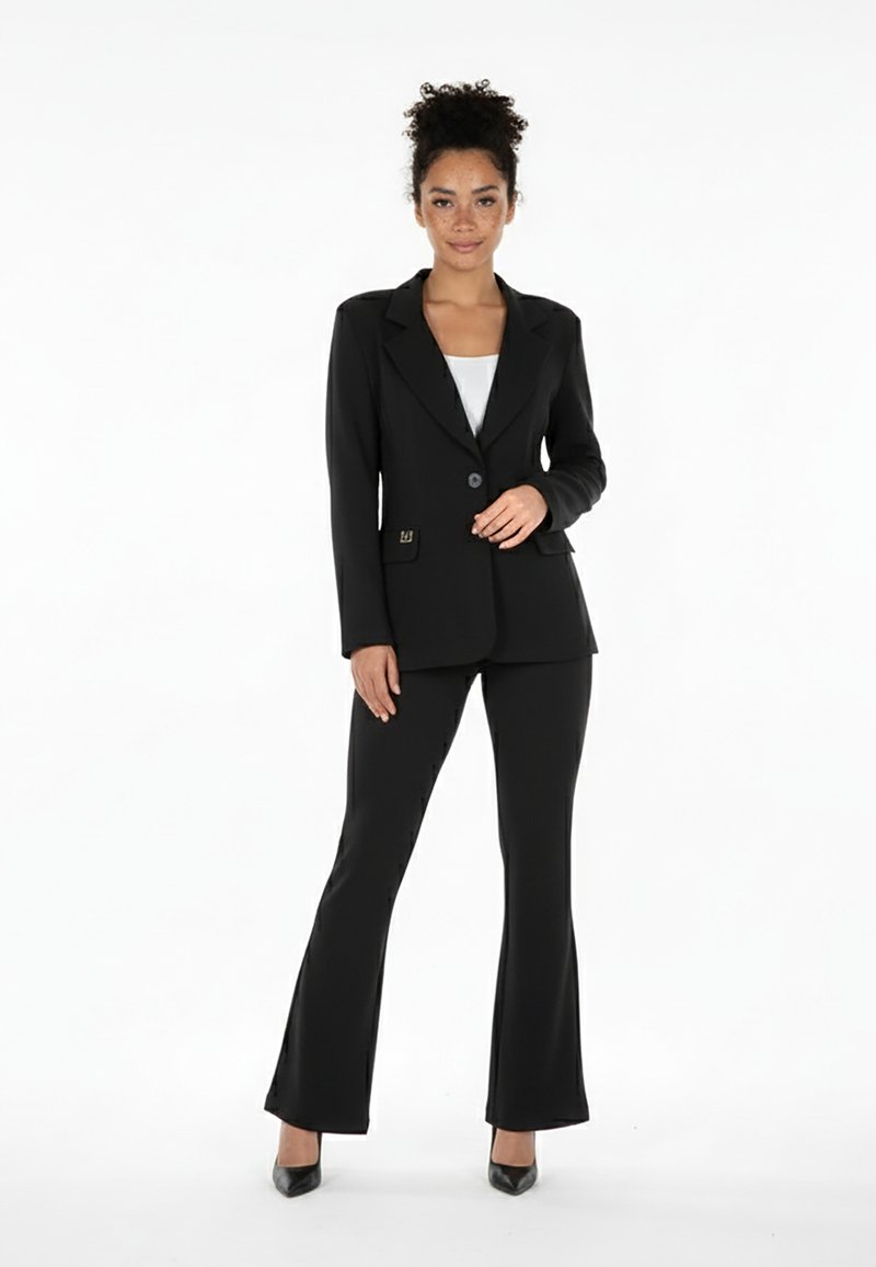 Czarny, dopasowany marynarka z pasującymi, rozszerzanymi spodniami. Gładki materiał, zapięcie na jeden guzik, dwie kieszenie i subtelne akcenty. Buty na wysokim obcasie.
