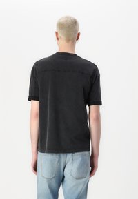 Svart t-shirt med kort ärm och avslappnad passform, med rundad halsringning och en något texturerad yta. Kombinerad med ljusblå jeans.