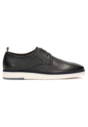Chaussure noire en cuir texturé à lacets, semelle blanche striée et languette en tissu rouge, blanche et bleue au talon, vue de profil.