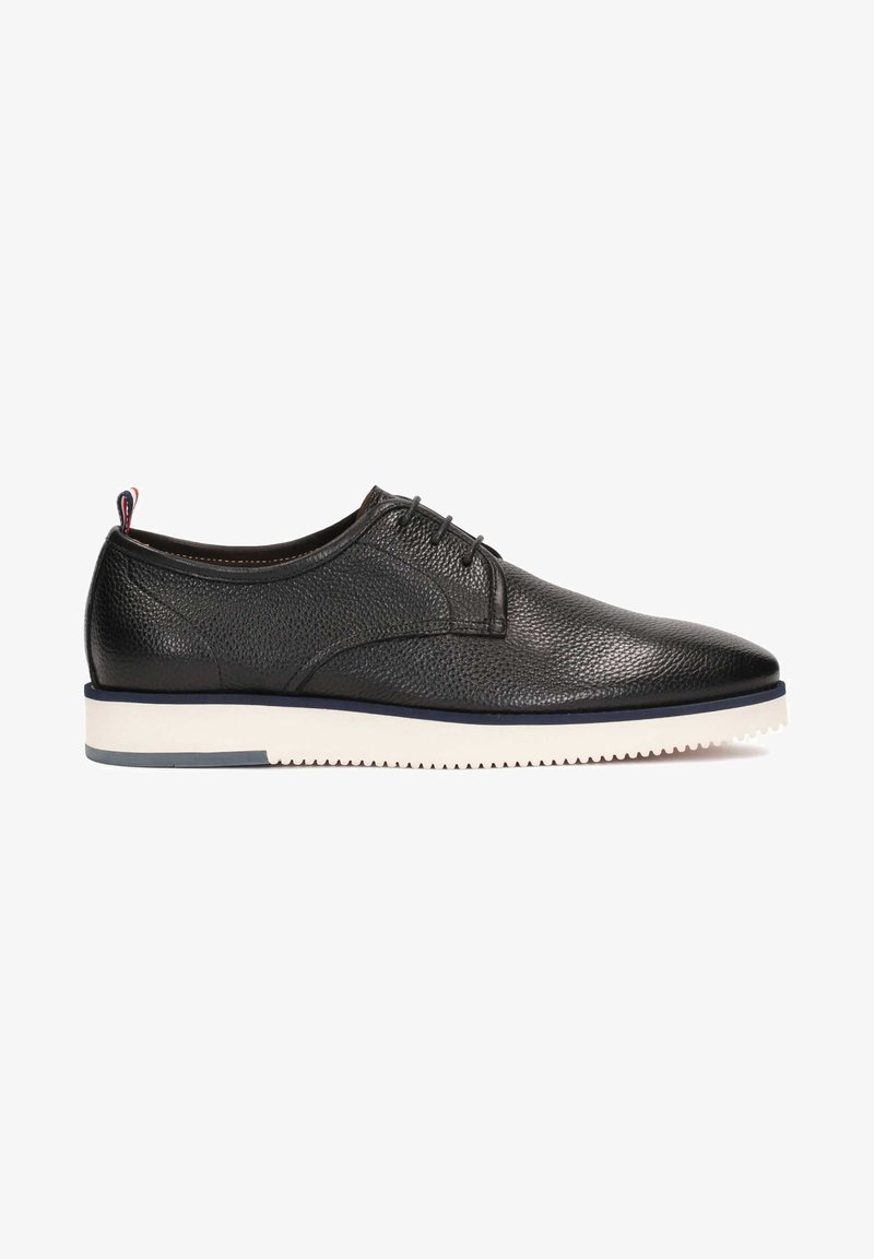 Chaussure noire en cuir texturé à lacets, semelle blanche striée et languette en tissu rouge, blanche et bleue au talon, vue de profil.