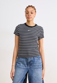 Μαύρο και λευκό ριγέ T-shirt με στρογγυλή λαιμόκοψη και κοντά μανίκια, που διαθέτει ένα μικρό λογότυπο της Nike στο στήθος. Συνδυασμένο με μπλε τζιν.