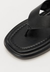 Must musta flip-flop sandaalid musta nahast, tekstureeritud ülemise osaga, pehme sisetallaga ja siledast ristkülikukujulisest tallast. Minimalistlik disain koos õmbluste detailidega.