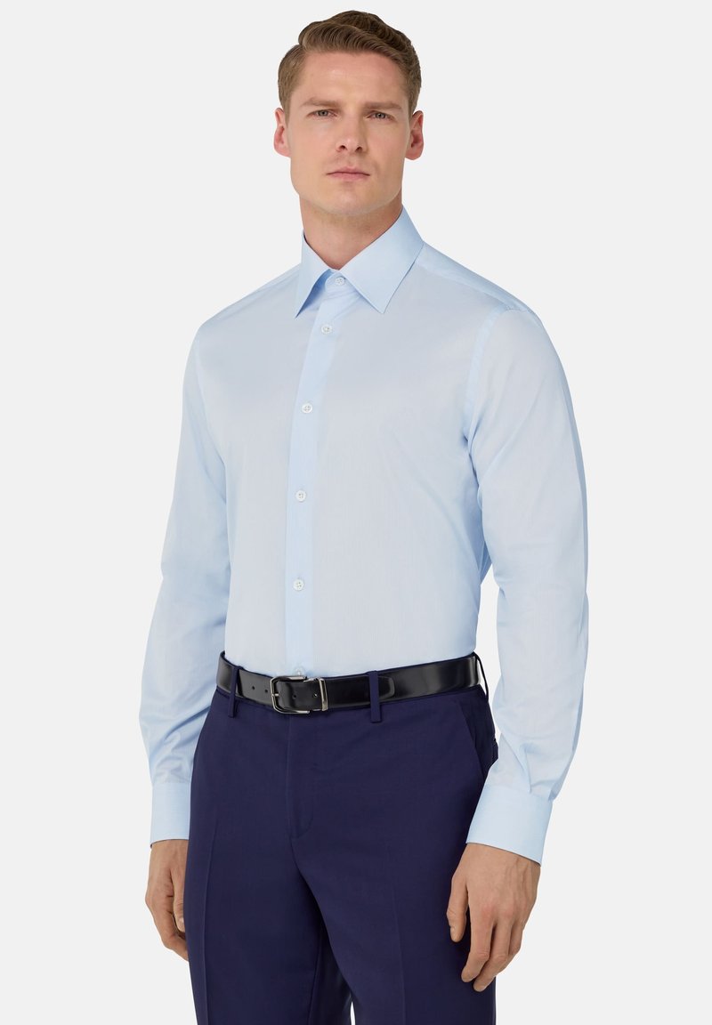 Camicia azzurro chiaro con colletto a punta, pattina dei bottoni e maniche lunghe. Abbinata a pantaloni blu navy e una cintura nera.