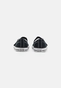 Zapatillas de lona negras con costuras blancas, suelas de goma y un diseño bajo. Presentan una pestaña en el talón trasero y la marca "Converse All Star".