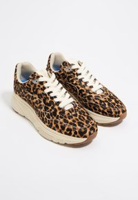Leopard print sneakers with beige rubber soles, white laces, and a textured fabric upper. Notable for bold pattern and cushioned design.