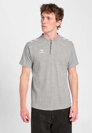 Mand iført en lysegrå kortærmet sportstrøje med ståkrave og sorte bukser, der kigger til venstre.