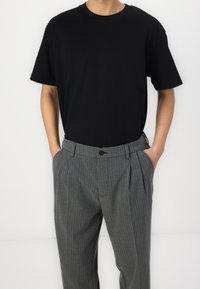 T-shirt nera a maniche corte abbinata a pantaloni grigi a righe sottili. I pantaloni hanno pieghe frontali e chiusura con bottone. Tessuto di cotone liscio.