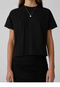 T-shirt in cotone nero a maniche corte con orli arrotolati, scollatura tonda e vestibilità morbida, abbinato a una gonna nera aderente.