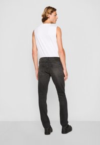 Vaqueros negros ajustados con una cintura de altura media, bolsillos traseros y textura suave. Combinados con una camiseta sin mangas blanca y calzado negro.