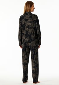 Black pajama set with a ginkgo leaf pattern in gold. Long-sleeved shirt and loose-fitting pants. Soft fabric, relaxed fit, and smooth texture.