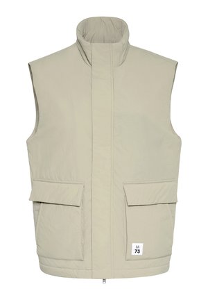 Ljusbeige ärmlös vadderad väst med hög krage, framslte dragkedja täckt av klaff, två stora fickor med klaffar och liten "M 73"-etikett.